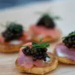 Small pieces of bread and meat with black caviar on top