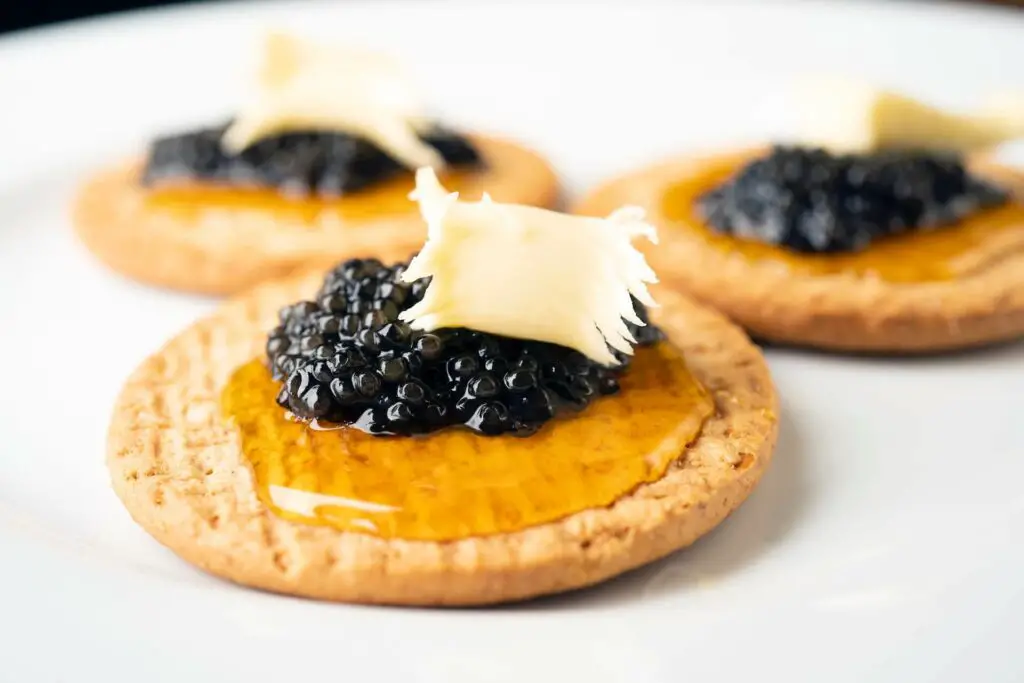 Dark caviar on top of a cracker with some honey and cheese