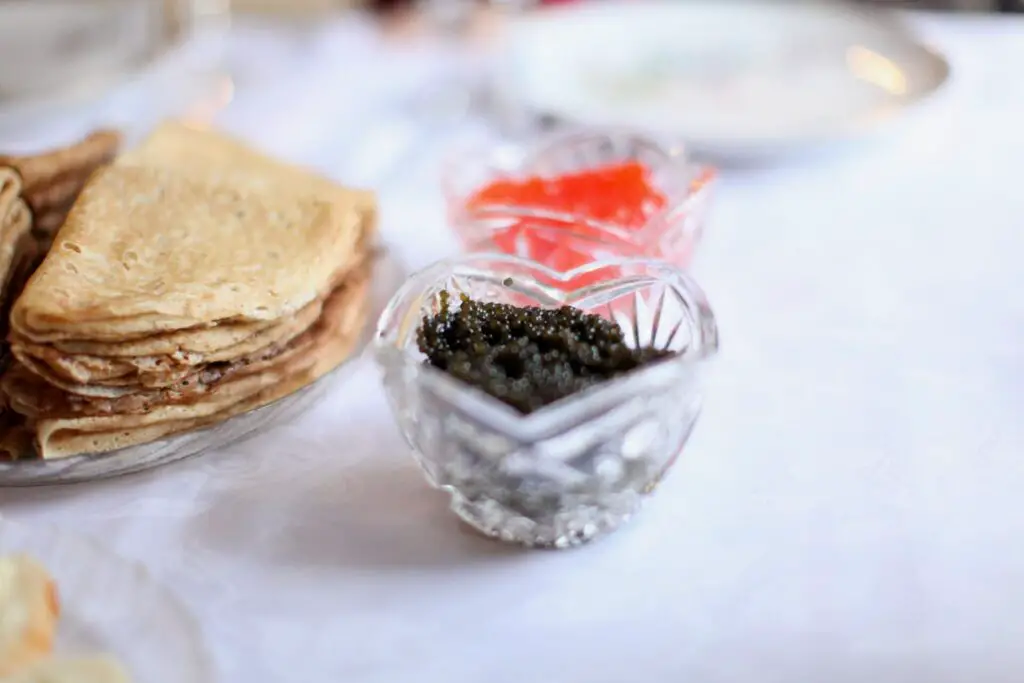 A tiny bowl of dark caviar next to some crepes