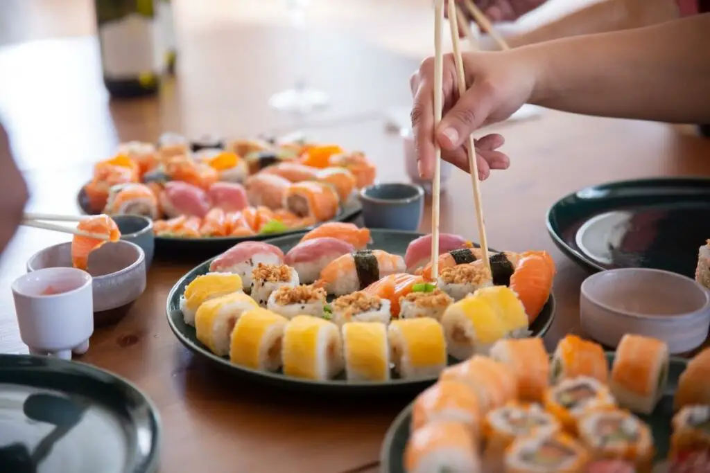 A person holding chopsticks with sushi on a plate